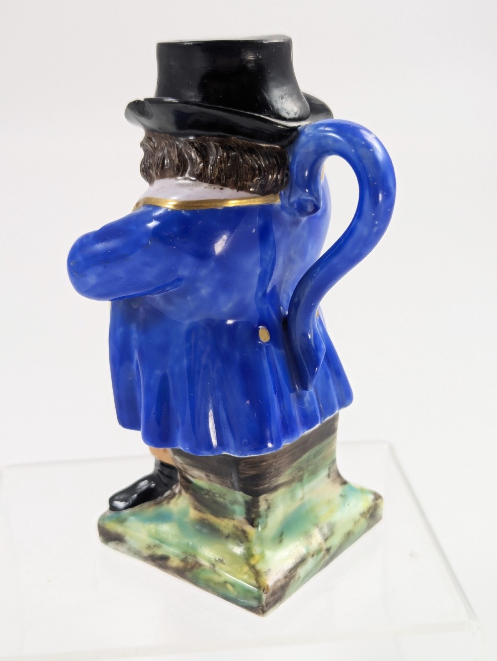A porcelain Toby jug depicting a gentleman in a black top hat, blue coat, and striped trousers taking snuff. View III