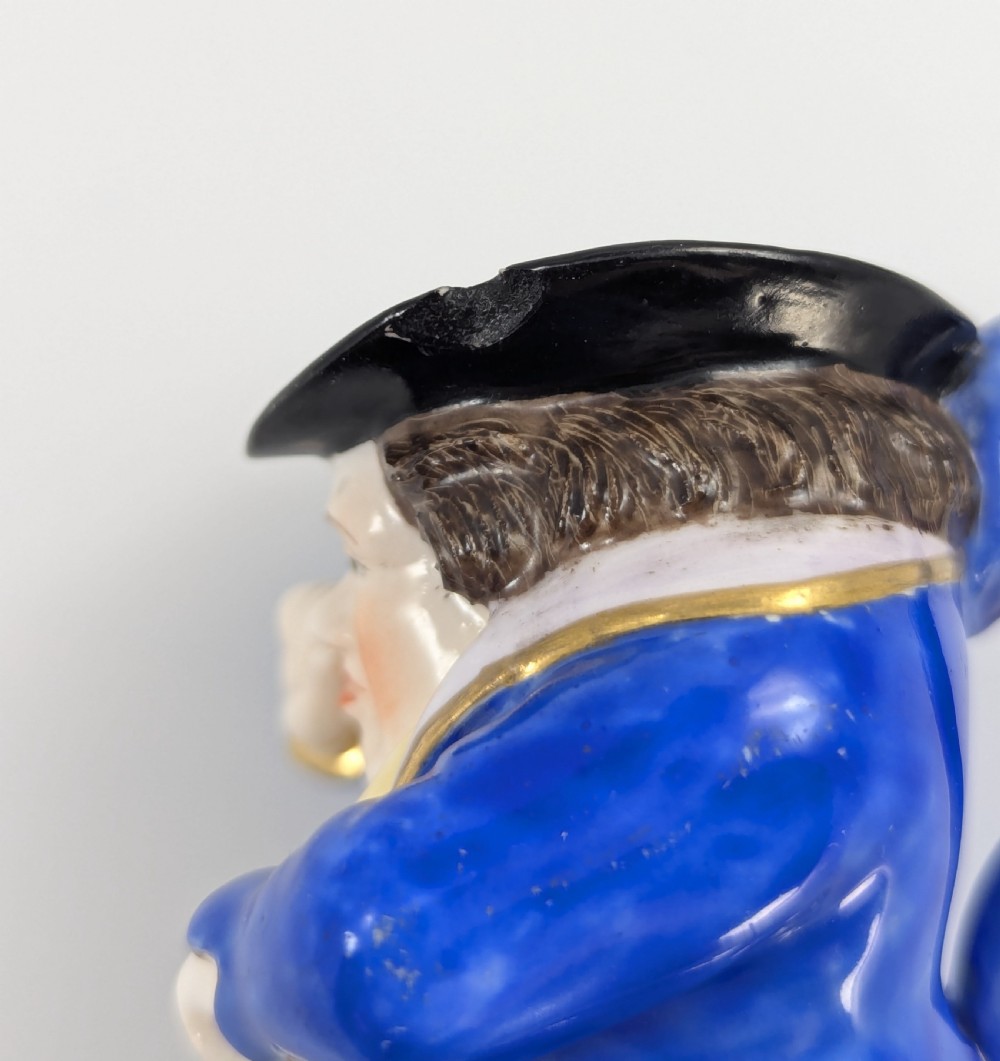 A porcelain Toby jug depicting a gentleman in a black top hat, blue coat, and striped trousers taking snuff. View VIII