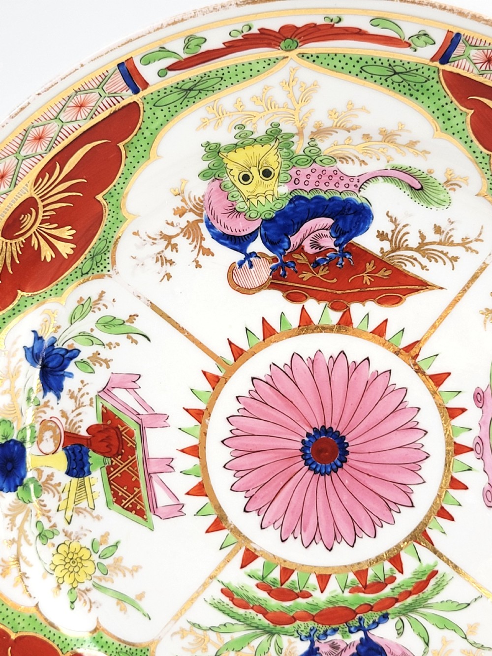 A circular antique English porcelain dessert plate decorated with hand-painted Chinoiserie panels, mythical dragons, and a pink central flower motif. View V