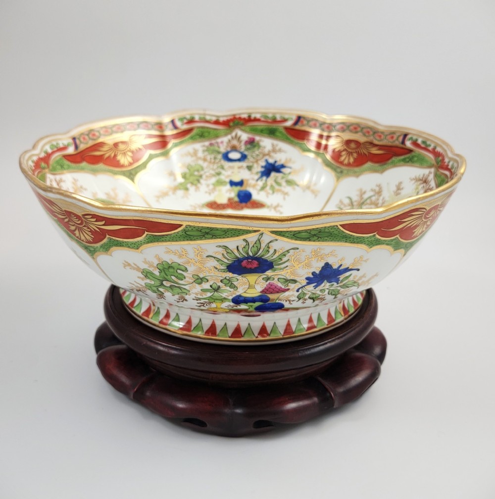 A Regency Chamberlain Worcester porcelain bowl with scalloped edges and colourful Chinoiserie enamel painting, resting on a carved dark mahogany stand.