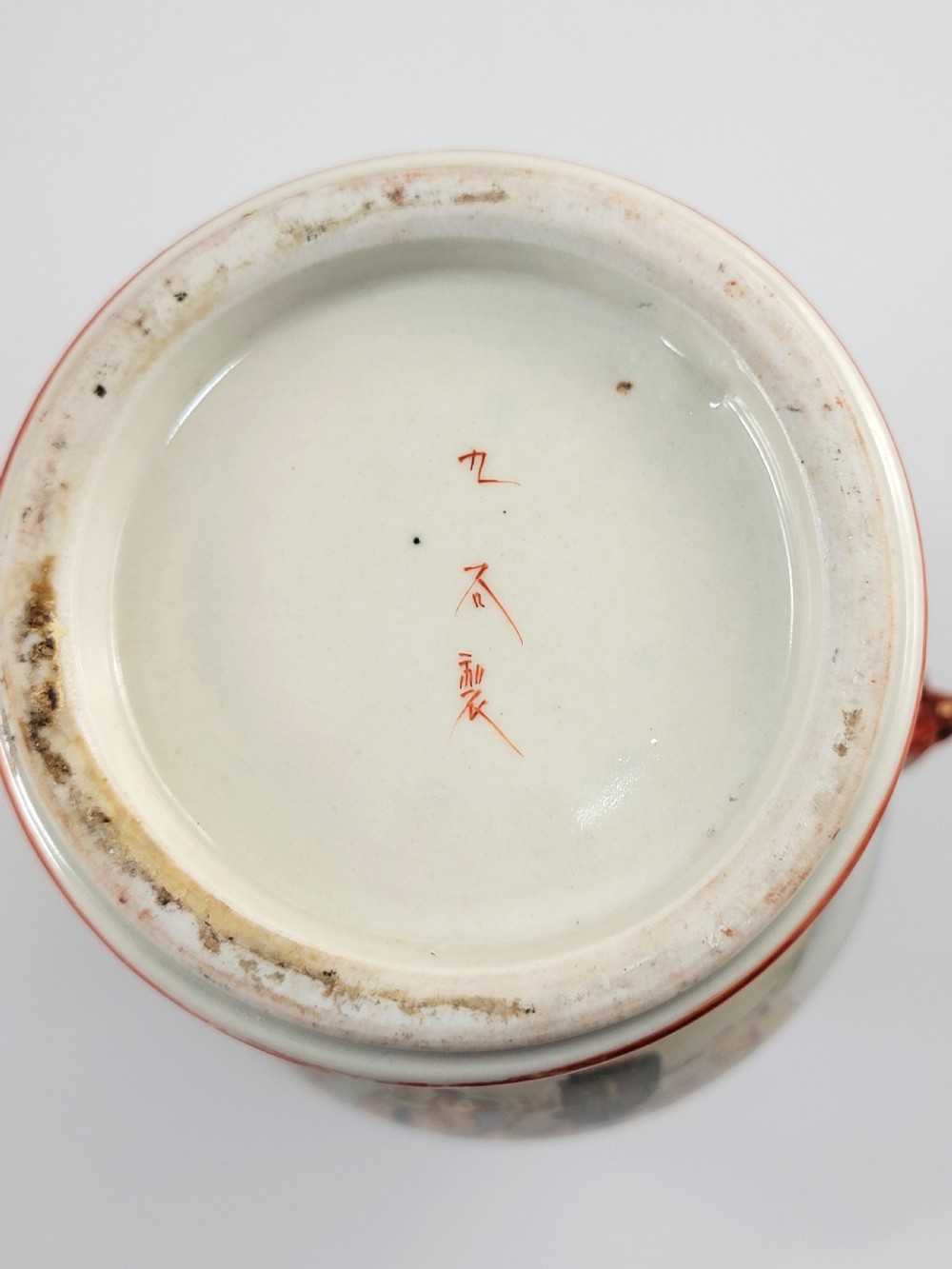An antique Japanese Kutani porcelain vase featuring hand-painted figures, iron-red flared rim, gilded highlights, moulded lion handles, and a carved wooden display stand. View X