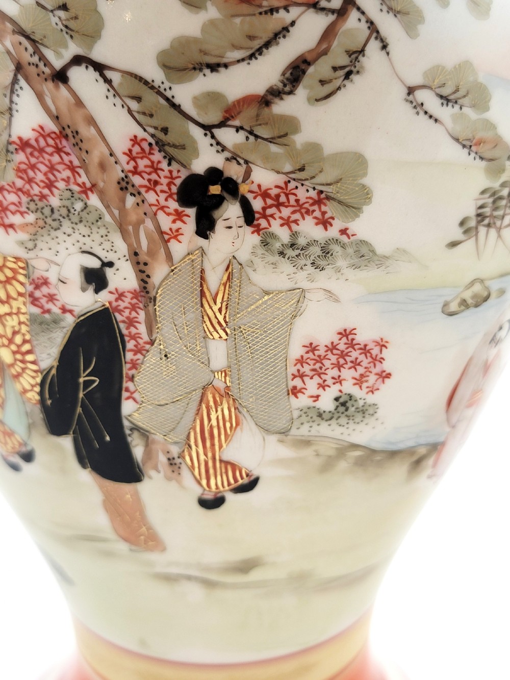 An antique Japanese Kutani porcelain vase featuring hand-painted figures, iron-red flared rim, gilded highlights, moulded lion handles, and a carved wooden display stand. View XV