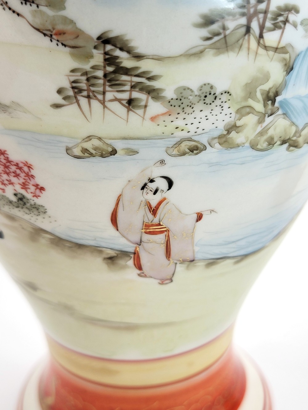 An antique Japanese Kutani porcelain vase featuring hand-painted figures, iron-red flared rim, gilded highlights, moulded lion handles, and a carved wooden display stand. View XVI