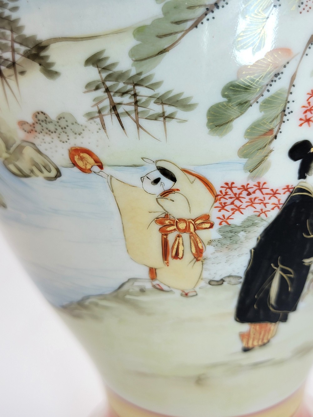 An antique Japanese Kutani porcelain vase featuring hand-painted figures, iron-red flared rim, gilded highlights, moulded lion handles, and a carved wooden display stand. View XVII