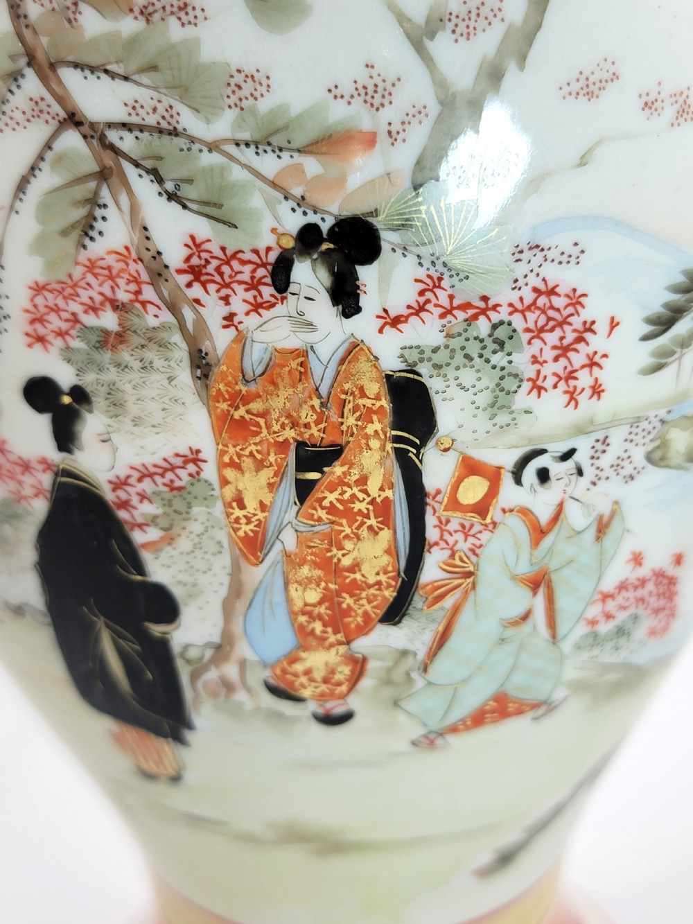 An antique Japanese Kutani porcelain vase featuring hand-painted figures, iron-red flared rim, gilded highlights, moulded lion handles, and a carved wooden display stand. View XVIII