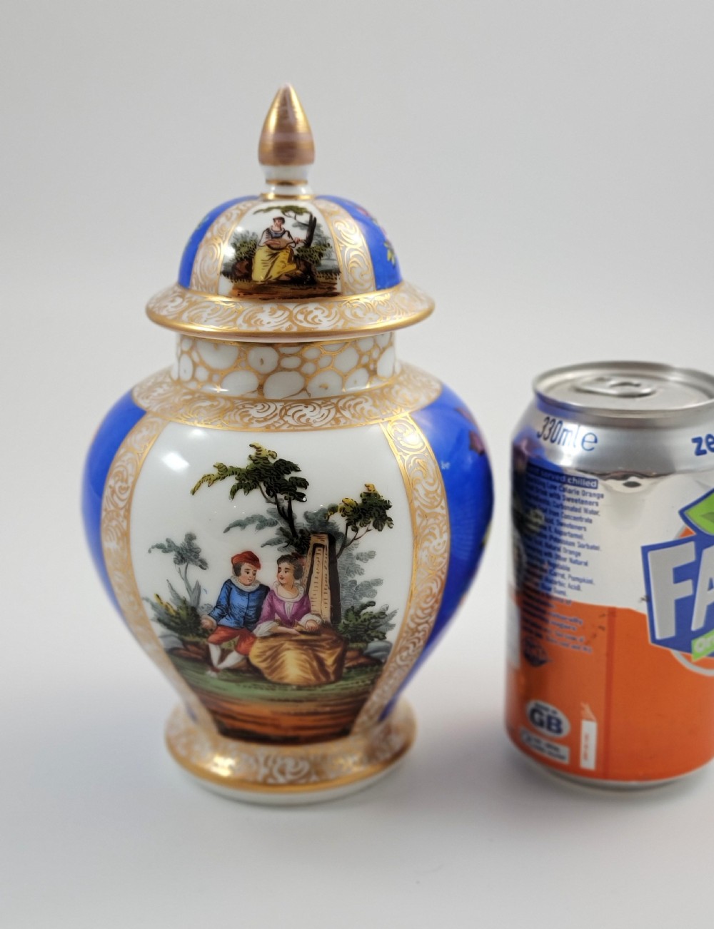 A lidded Dresden porcelain ginger jar featuring hand-painted courting scenes inside gilded cartouches against a cobalt blue ground, topped with a pointed gilt finial. View VIII