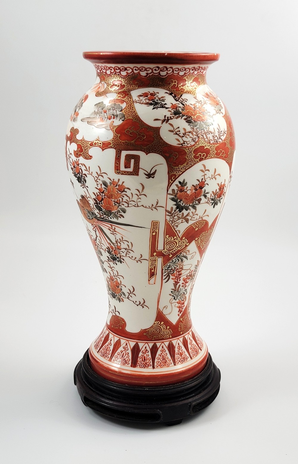 A baluster-shaped Japanese Kutani porcelain vase decorated with red and gold floral motifs on a carved dark wood base.