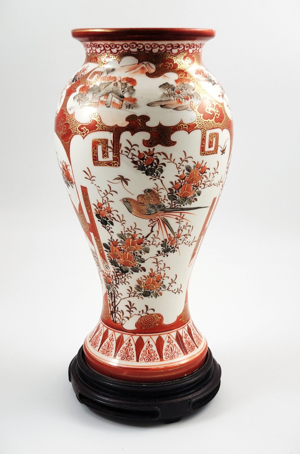 A baluster-shaped Japanese Kutani porcelain vase decorated with red and gold floral motifs on a carved dark wood base. View II