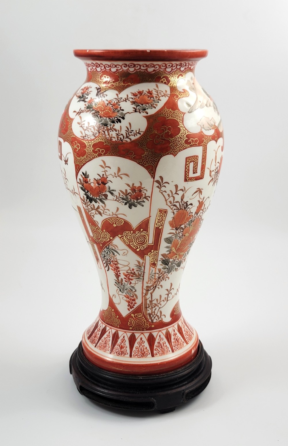 A baluster-shaped Japanese Kutani porcelain vase decorated with red and gold floral motifs on a carved dark wood base. View III