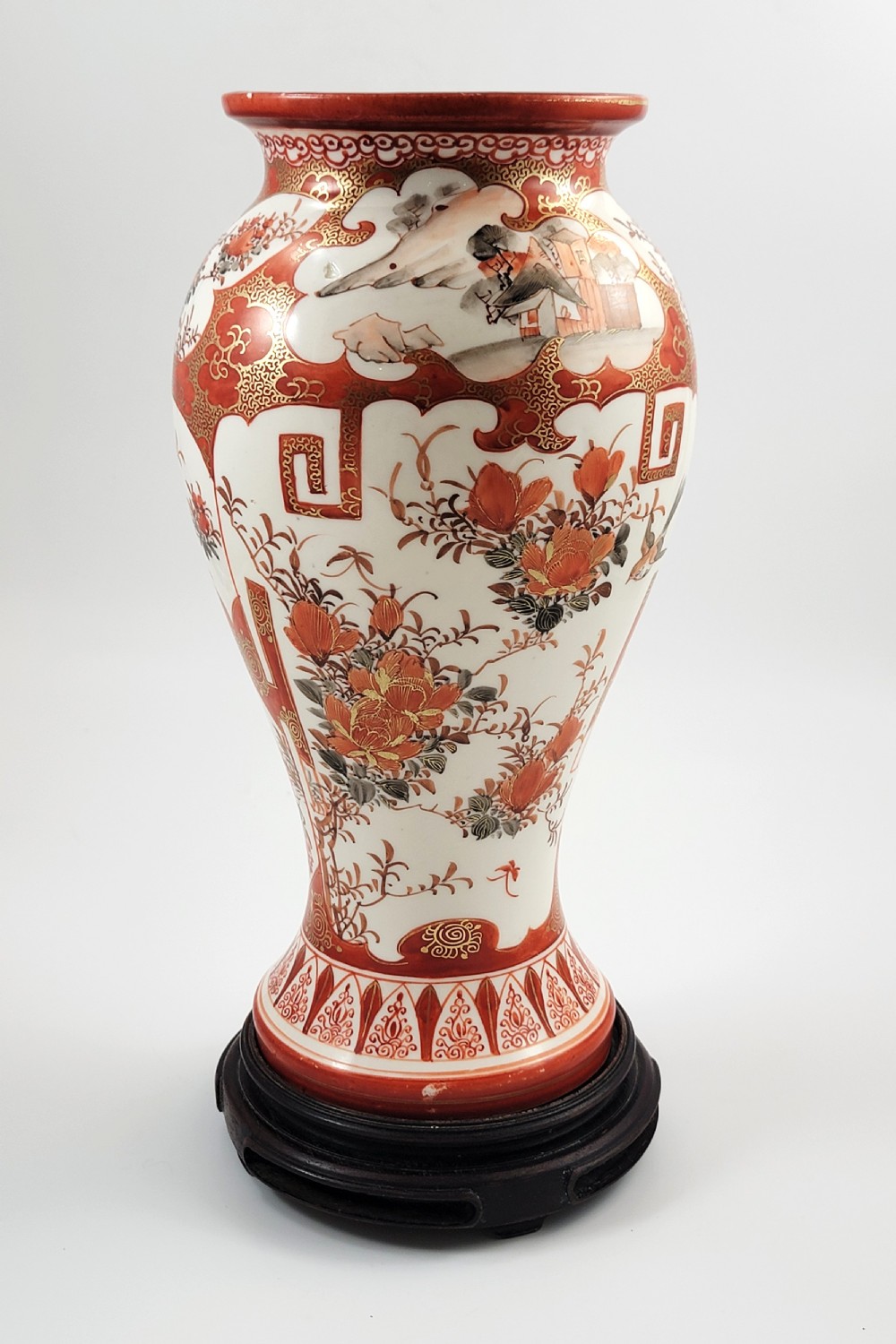 A baluster-shaped Japanese Kutani porcelain vase decorated with red and gold floral motifs on a carved dark wood base. View IV