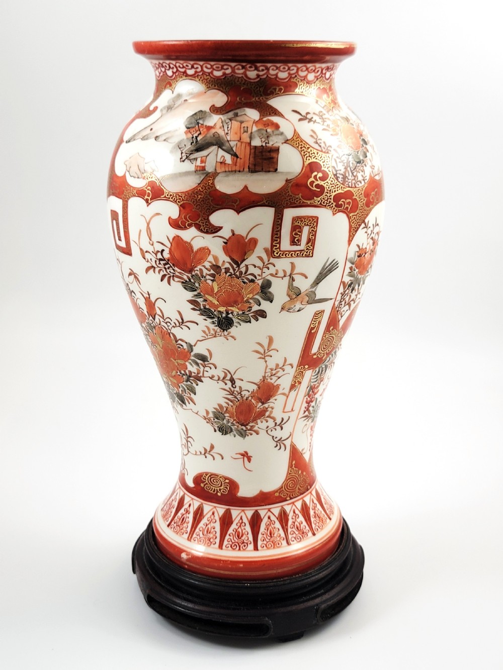 A baluster-shaped Japanese Kutani porcelain vase decorated with red and gold floral motifs on a carved dark wood base. View V