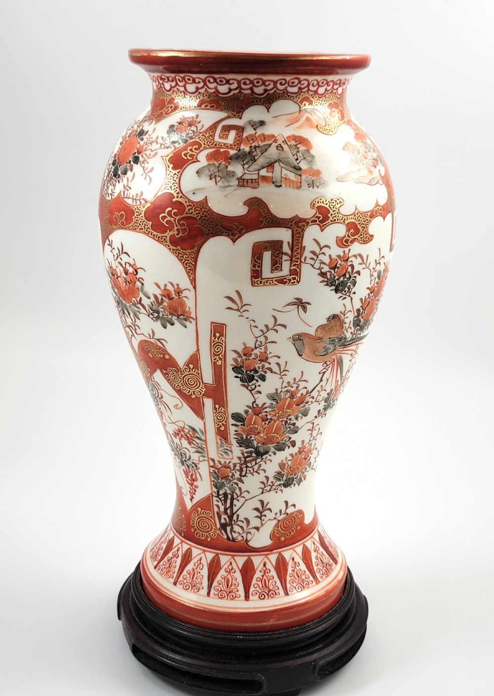 A baluster-shaped Japanese Kutani porcelain vase decorated with red and gold floral motifs on a carved dark wood base. View VII