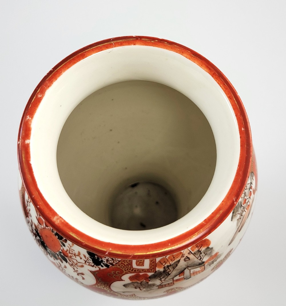 A baluster-shaped Japanese Kutani porcelain vase decorated with red and gold floral motifs on a carved dark wood base. View VIII
