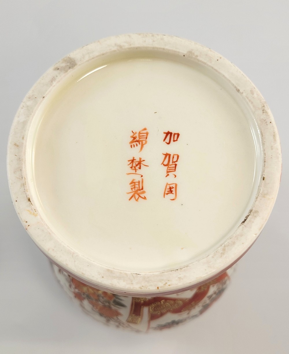 A baluster-shaped Japanese Kutani porcelain vase decorated with red and gold floral motifs on a carved dark wood base. View IX