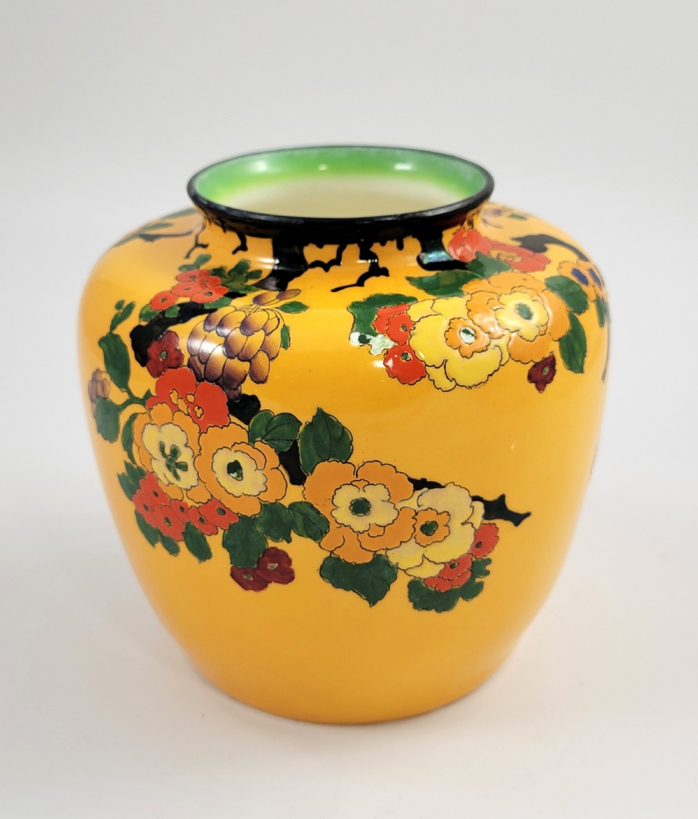 A round yellow glazed ceramic vase decorated with hand-painted polychrome floral blossoms on black branches with a green inner rim.