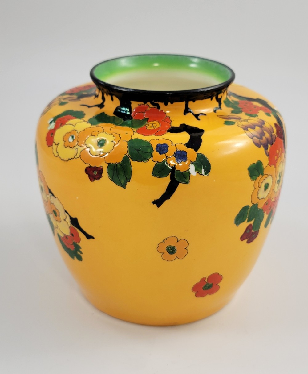 A round yellow glazed ceramic vase decorated with hand-painted polychrome floral blossoms on black branches with a green inner rim. View II