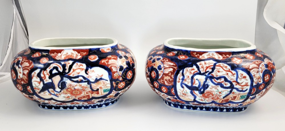 A pair of oval Japanese Imari porcelain jardinieres decorated with cobalt blue, iron red, and floral reserve panels.