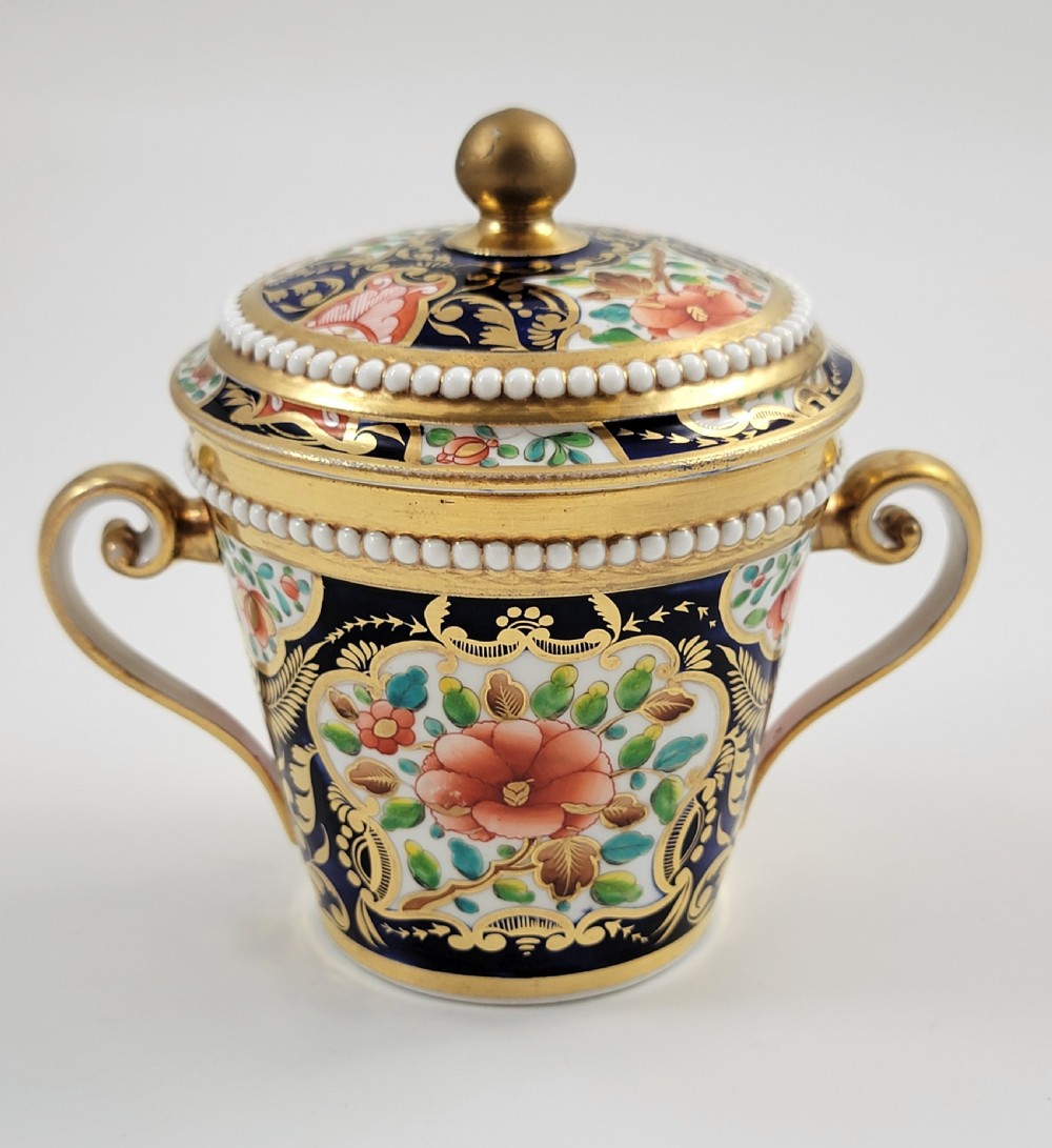 An antique porcelain chocolate cup and lid decorated with cobalt blue and gold Imari floral panels and raised white pearl borders.