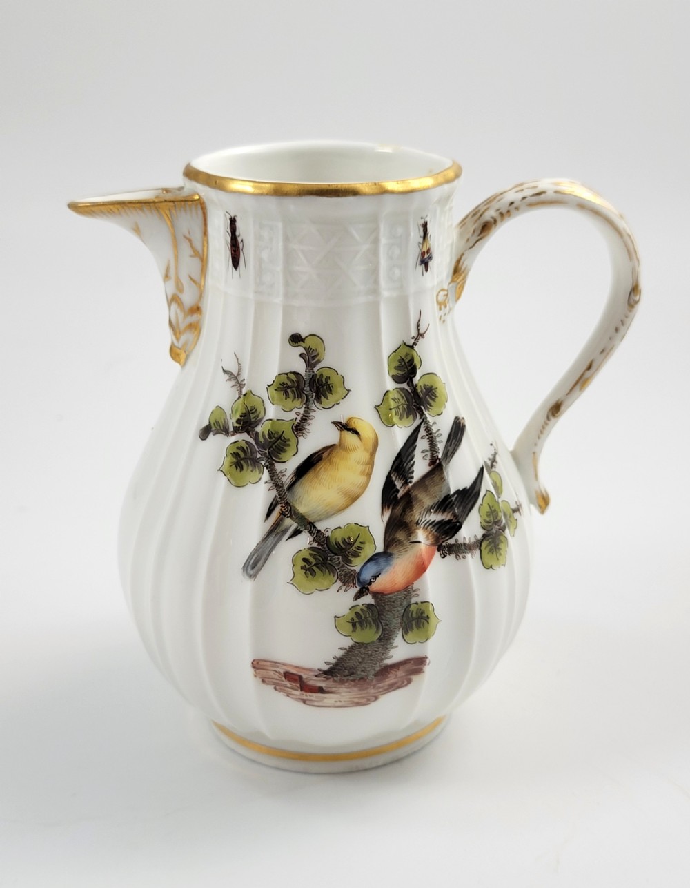 A white ribbed porcelain jug decorated with hand-painted birds, insects, and gilding along the spout and handle.