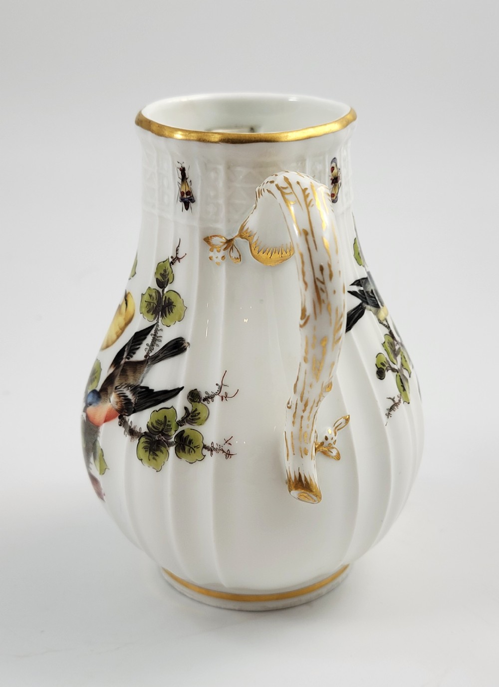A white ribbed porcelain jug decorated with hand-painted birds, insects, and gilding along the spout and handle. View II