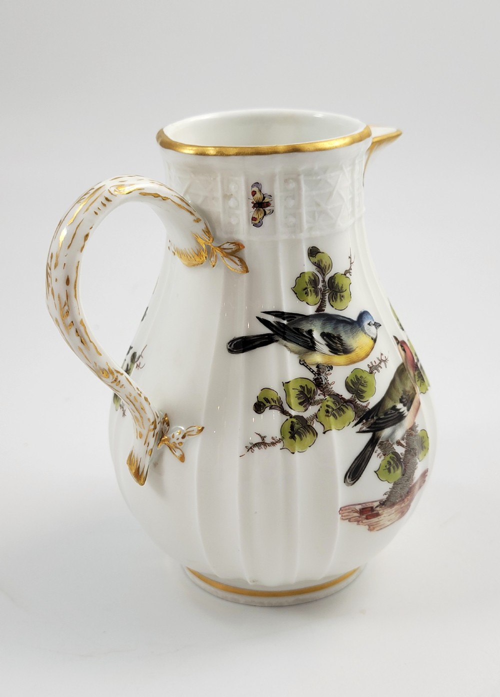 A white ribbed porcelain jug decorated with hand-painted birds, insects, and gilding along the spout and handle. View III