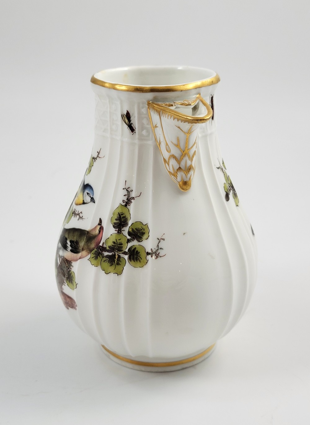 A white ribbed porcelain jug decorated with hand-painted birds, insects, and gilding along the spout and handle. View V