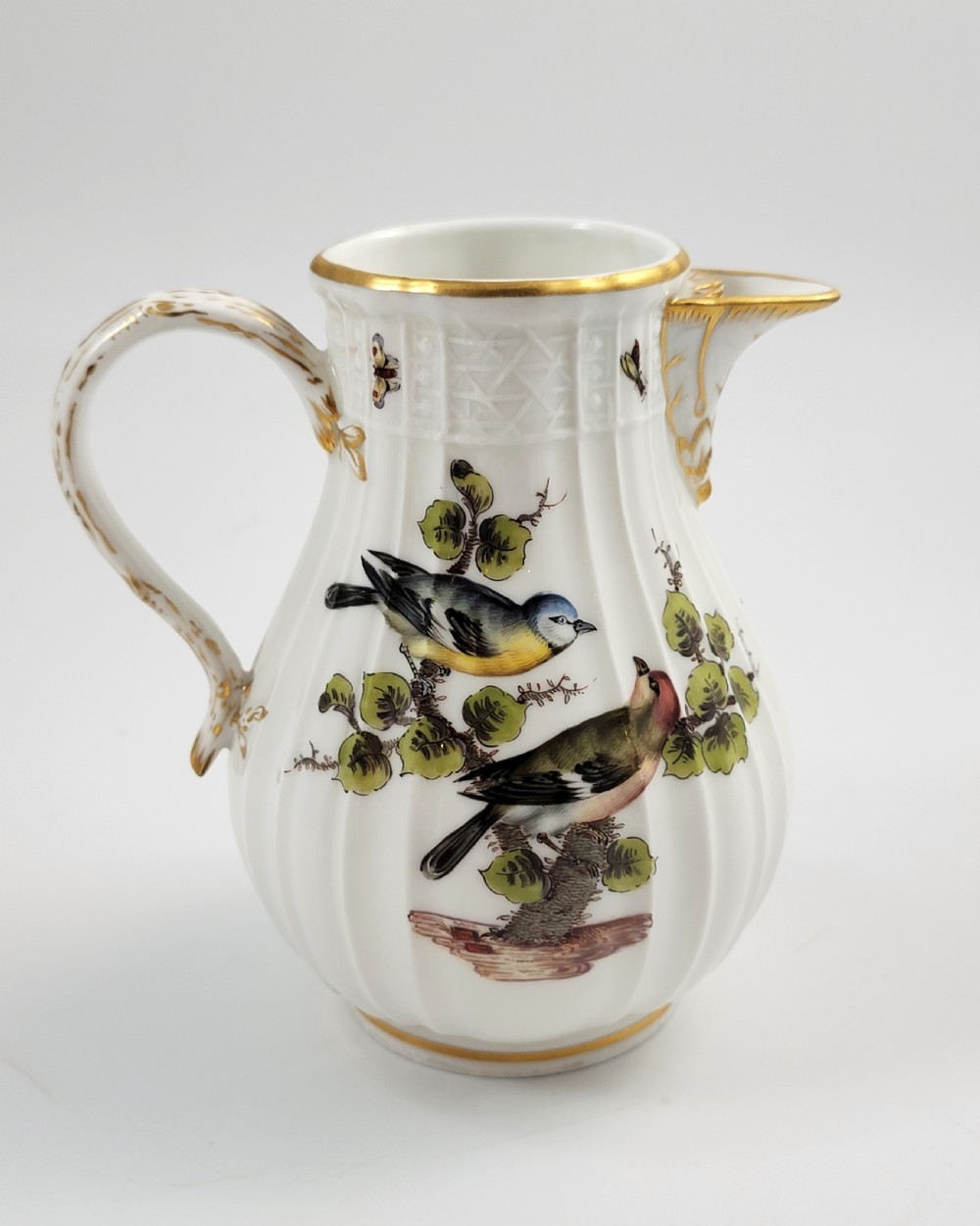 A white ribbed porcelain jug decorated with hand-painted birds, insects, and gilding along the spout and handle. View VI