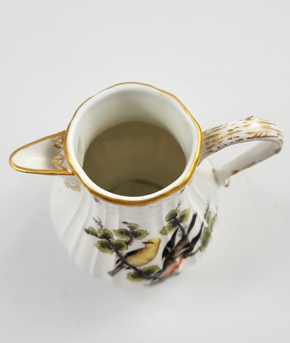 A white ribbed porcelain jug decorated with hand-painted birds, insects, and gilding along the spout and handle. View VII