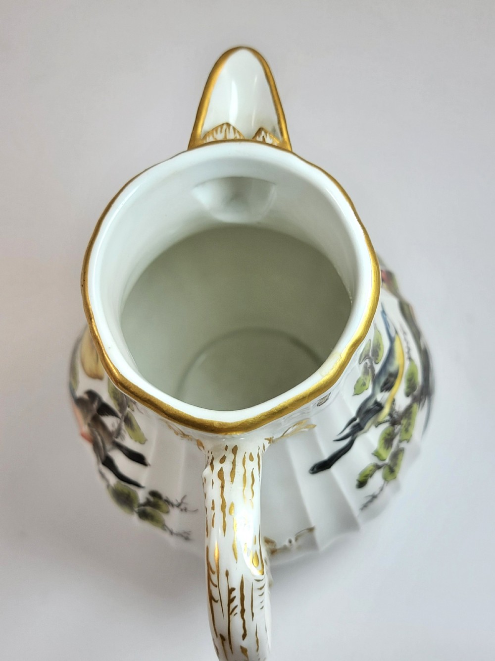 A white ribbed porcelain jug decorated with hand-painted birds, insects, and gilding along the spout and handle. View VIII