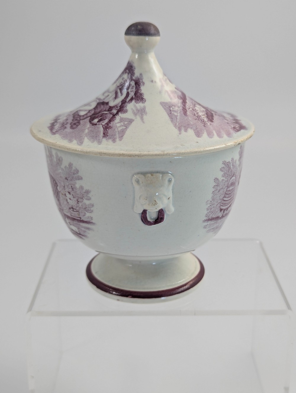 A 19th-century Staffordshire covered earthenware sugar bowl featuring a purple mulberry transferware romantic scene with lion mask handles and a pointed lid. View II
