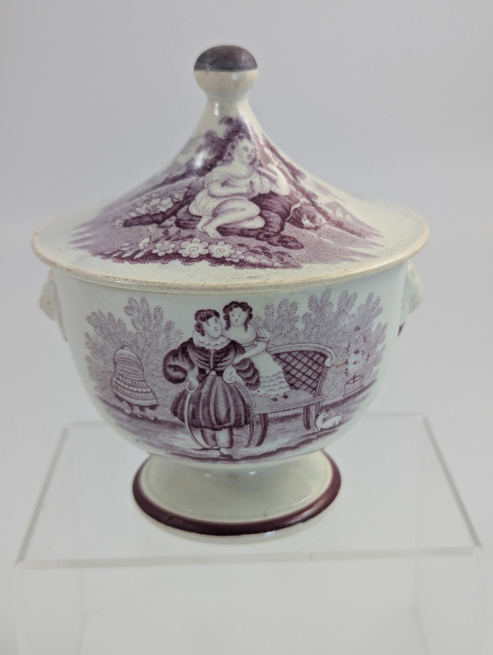 A 19th-century Staffordshire covered earthenware sugar bowl featuring a purple mulberry transferware romantic scene with lion mask handles and a pointed lid. View V