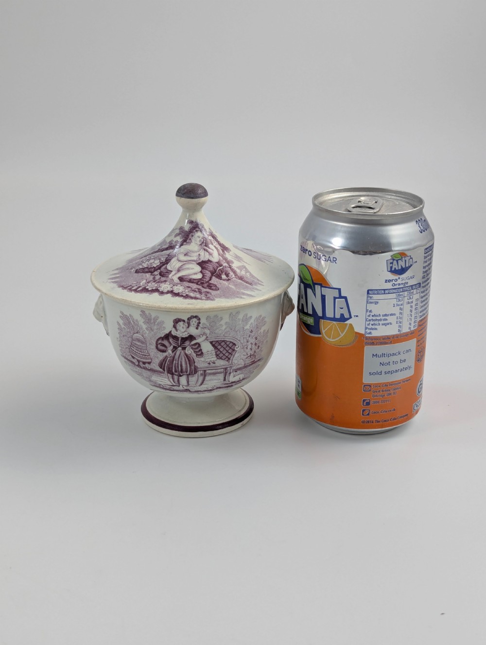 A 19th-century Staffordshire covered earthenware sugar bowl featuring a purple mulberry transferware romantic scene with lion mask handles and a pointed lid. View X
