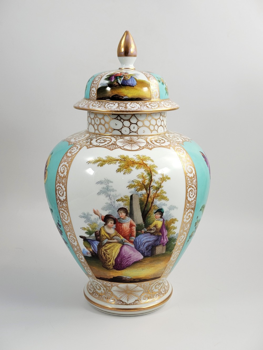 A 19th-century Dresden porcelain lidded vase featuring turquoise ground panels, gilded scrollwork, and hand-painted Watteau pastoral scenes.