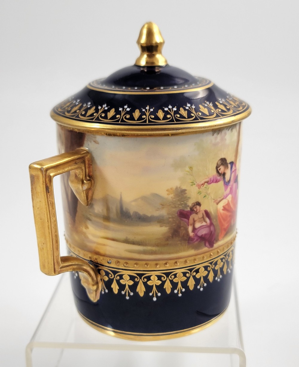 A cobalt blue porcelain covered cup featuring gold leaf scrollwork trim and a hand-painted allegorical woodland vignette with classical figures. View III