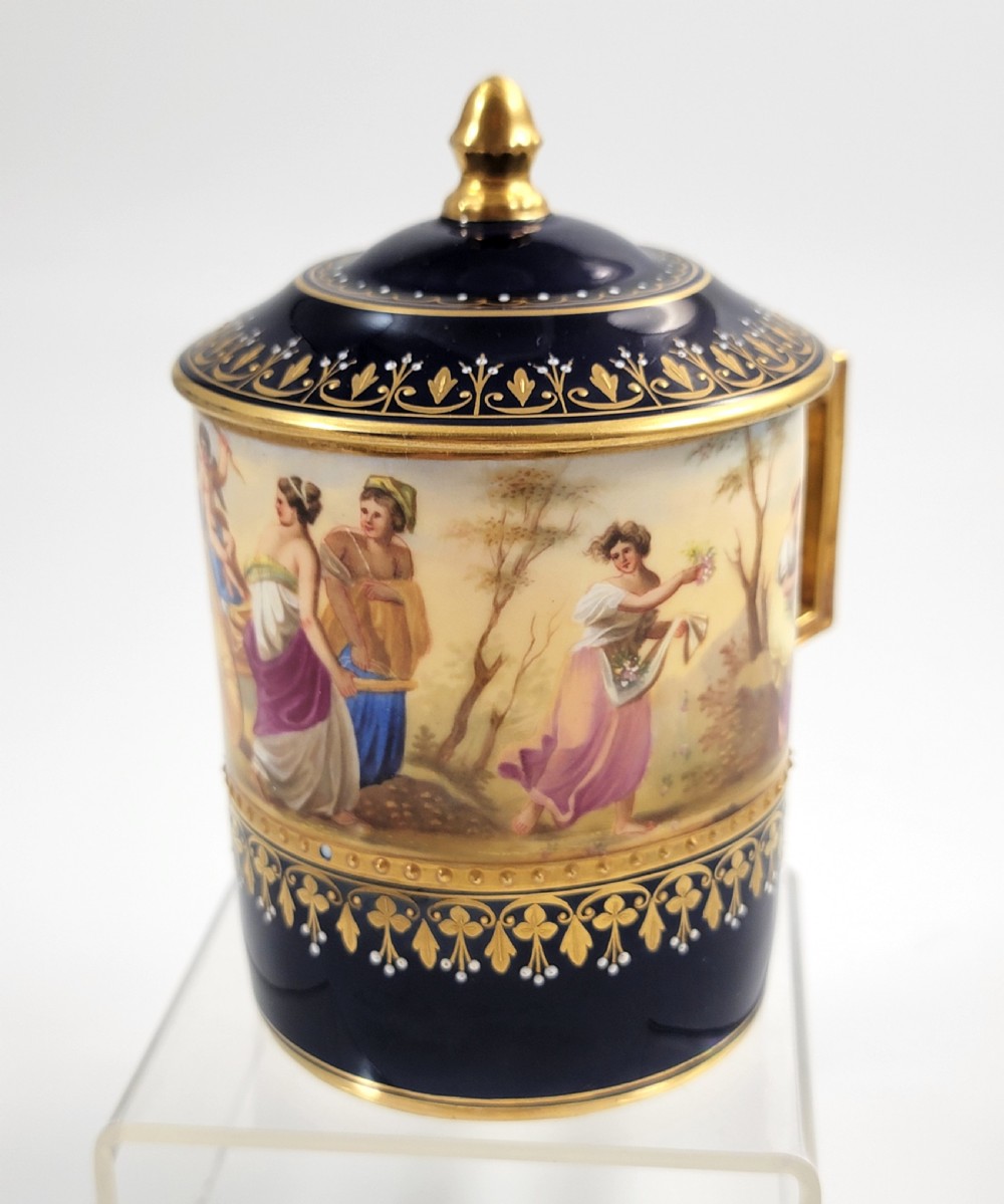 A cobalt blue porcelain covered cup featuring gold leaf scrollwork trim and a hand-painted allegorical woodland vignette with classical figures. View VII