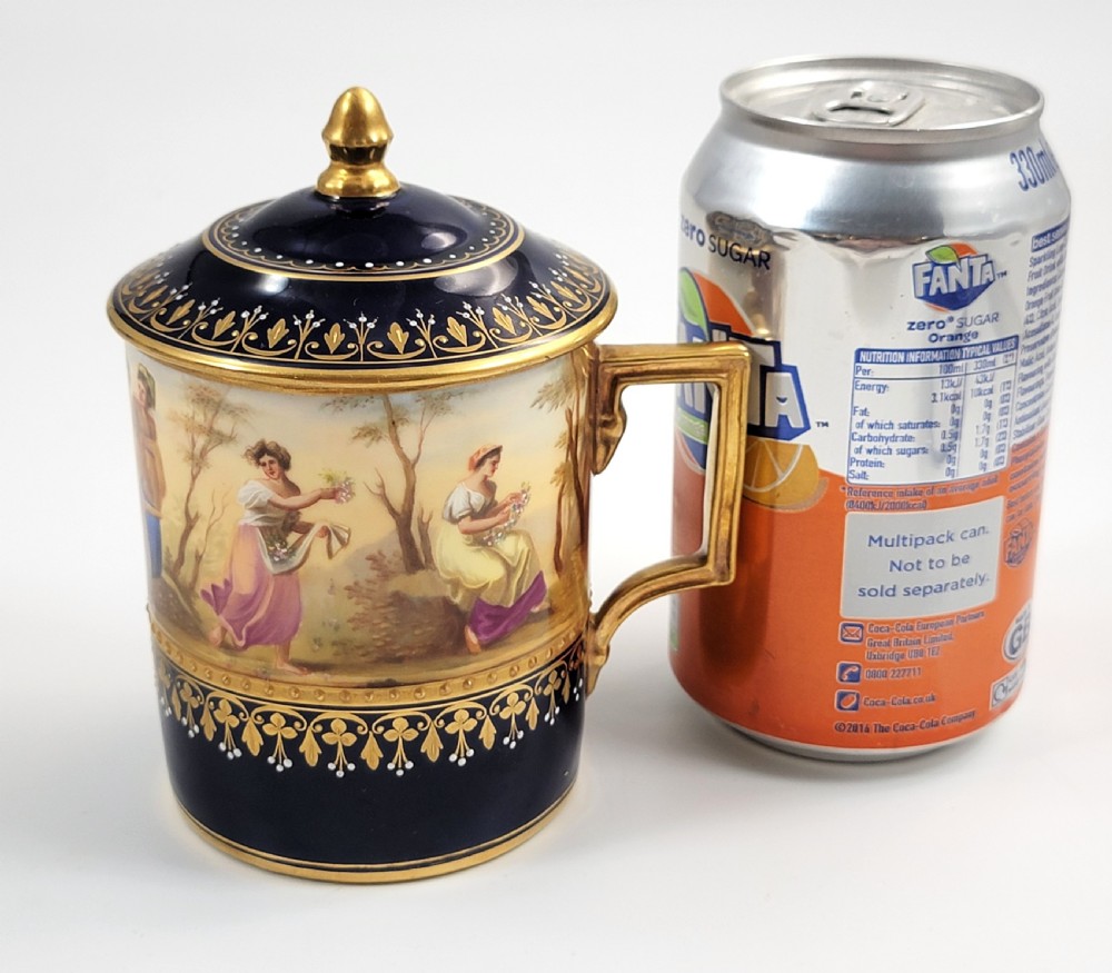 A cobalt blue porcelain covered cup featuring gold leaf scrollwork trim and a hand-painted allegorical woodland vignette with classical figures. View XI