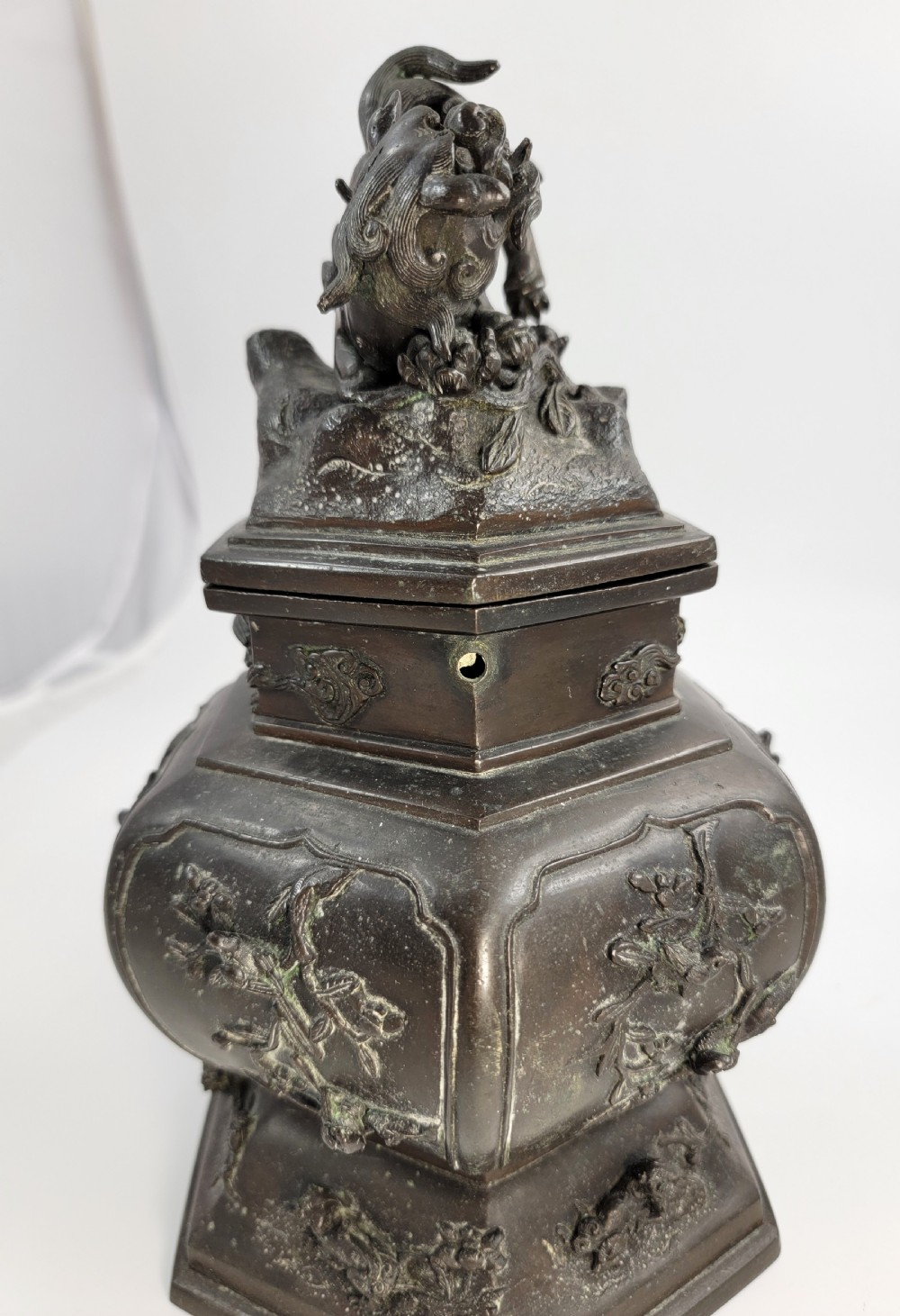 A dark patinated hexagonal bronze incense burner featuring floral relief panels and topped with a sculpted Fu lion finial. View VI