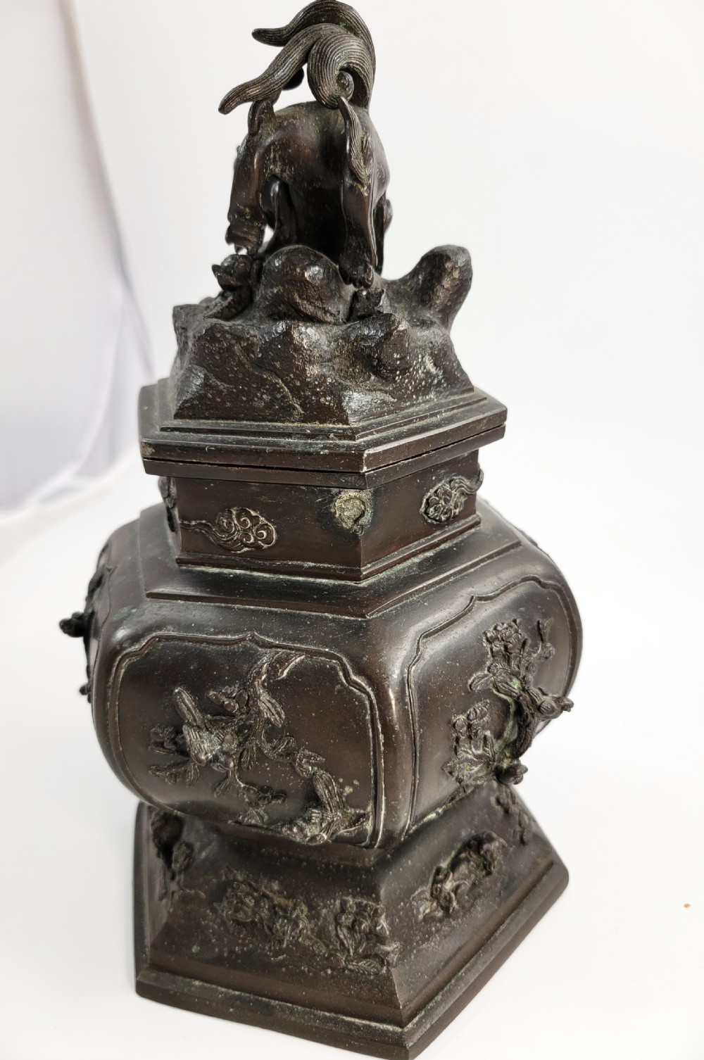 A dark patinated hexagonal bronze incense burner featuring floral relief panels and topped with a sculpted Fu lion finial. View VII