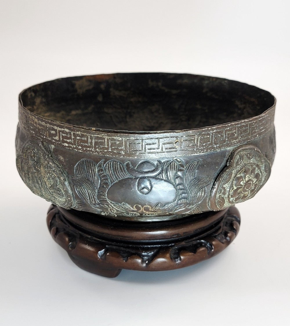 A patinated dark bronze Japanese bowl with carved archaic relief patterns and a key-fret border, resting on a carved wooden stand. View II