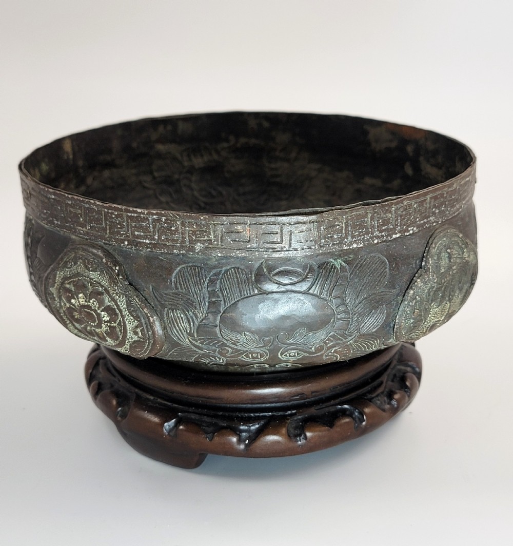 A patinated dark bronze Japanese bowl with carved archaic relief patterns and a key-fret border, resting on a carved wooden stand. View IV