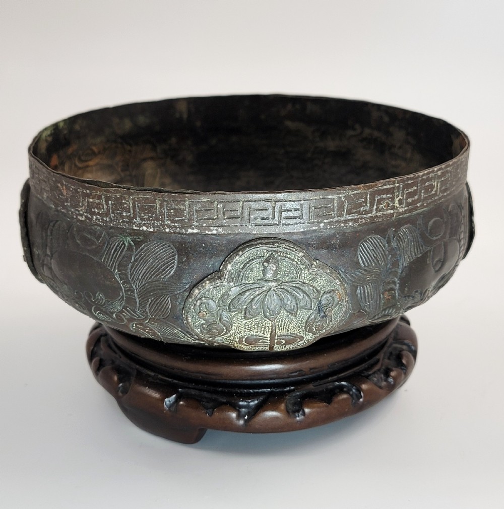 A patinated dark bronze Japanese bowl with carved archaic relief patterns and a key-fret border, resting on a carved wooden stand. View V
