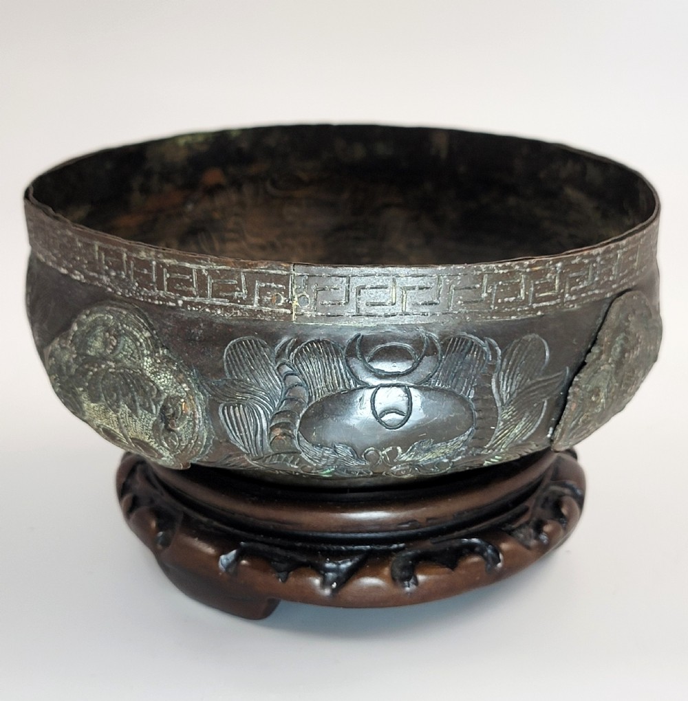 A patinated dark bronze Japanese bowl with carved archaic relief patterns and a key-fret border, resting on a carved wooden stand. View VI