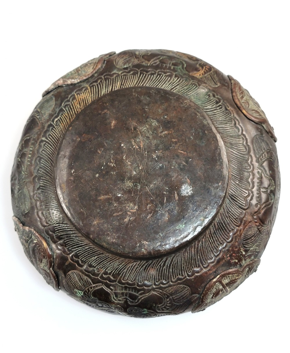 A patinated dark bronze Japanese bowl with carved archaic relief patterns and a key-fret border, resting on a carved wooden stand. View IX