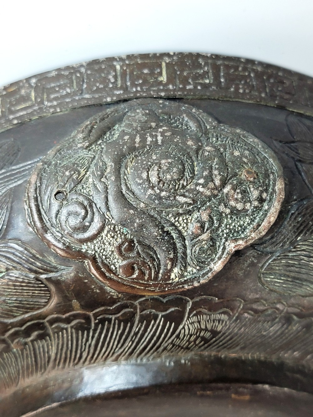 A patinated dark bronze Japanese bowl with carved archaic relief patterns and a key-fret border, resting on a carved wooden stand. View X