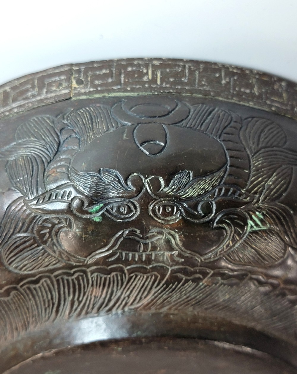 A patinated dark bronze Japanese bowl with carved archaic relief patterns and a key-fret border, resting on a carved wooden stand. View XI