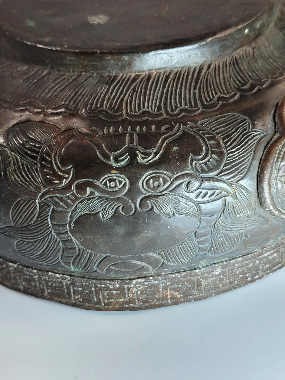 A patinated dark bronze Japanese bowl with carved archaic relief patterns and a key-fret border, resting on a carved wooden stand. View XIII