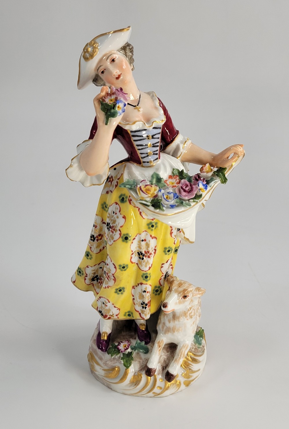A 19th-century German porcelain figure depicting a shepherdess in a yellow patterned skirt with a lamb resting at her feet. View VII