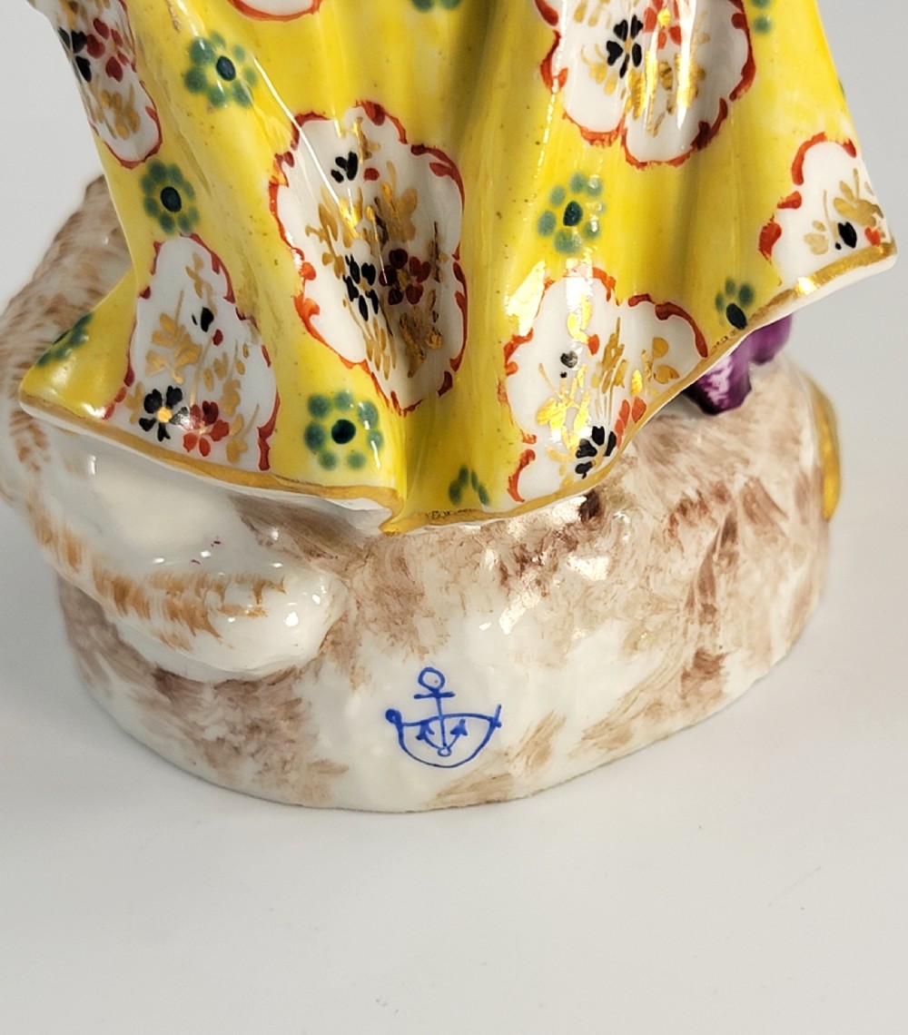 A 19th-century German porcelain figure depicting a shepherdess in a yellow patterned skirt with a lamb resting at her feet. View IX