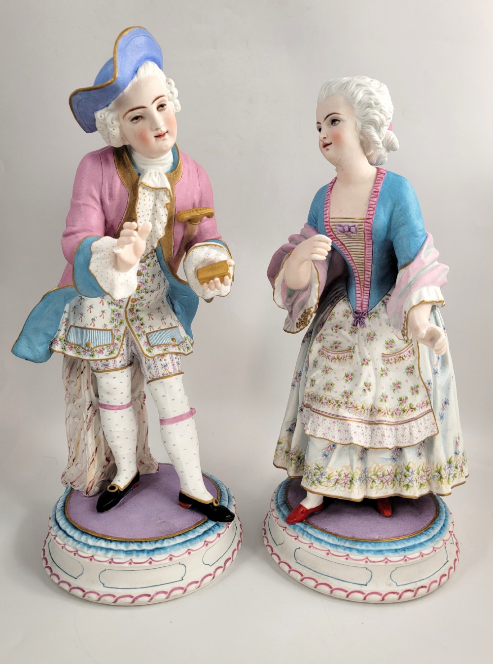 A pair of late 19th-century French biscuit porcelain figures depicting an 18th-century courtly man and woman with pastel pink and blue painted garments.