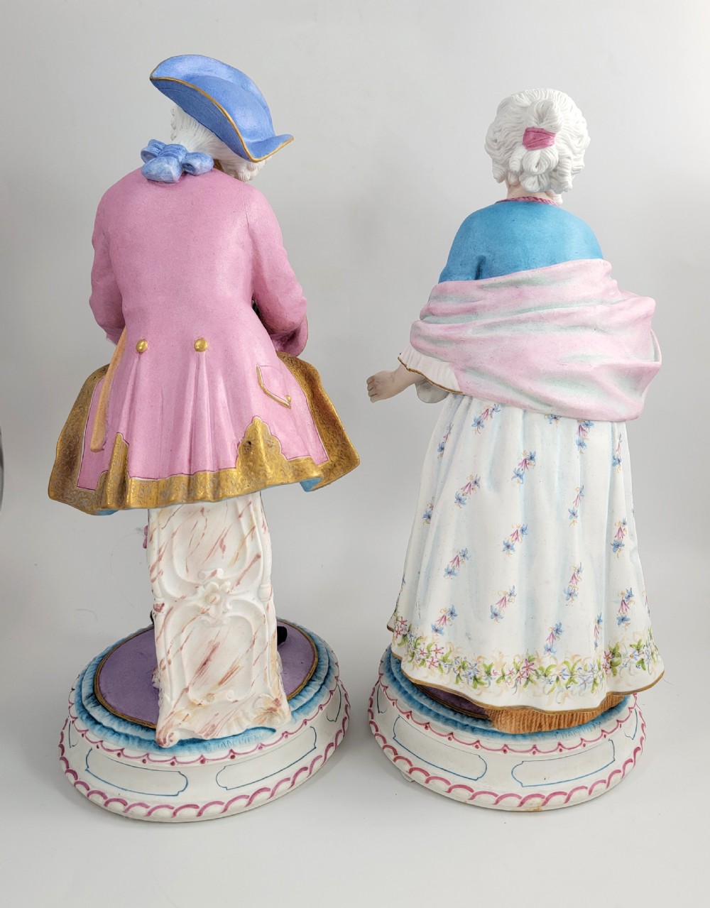 A pair of late 19th-century French biscuit porcelain figures depicting an 18th-century courtly man and woman with pastel pink and blue painted garments. View V